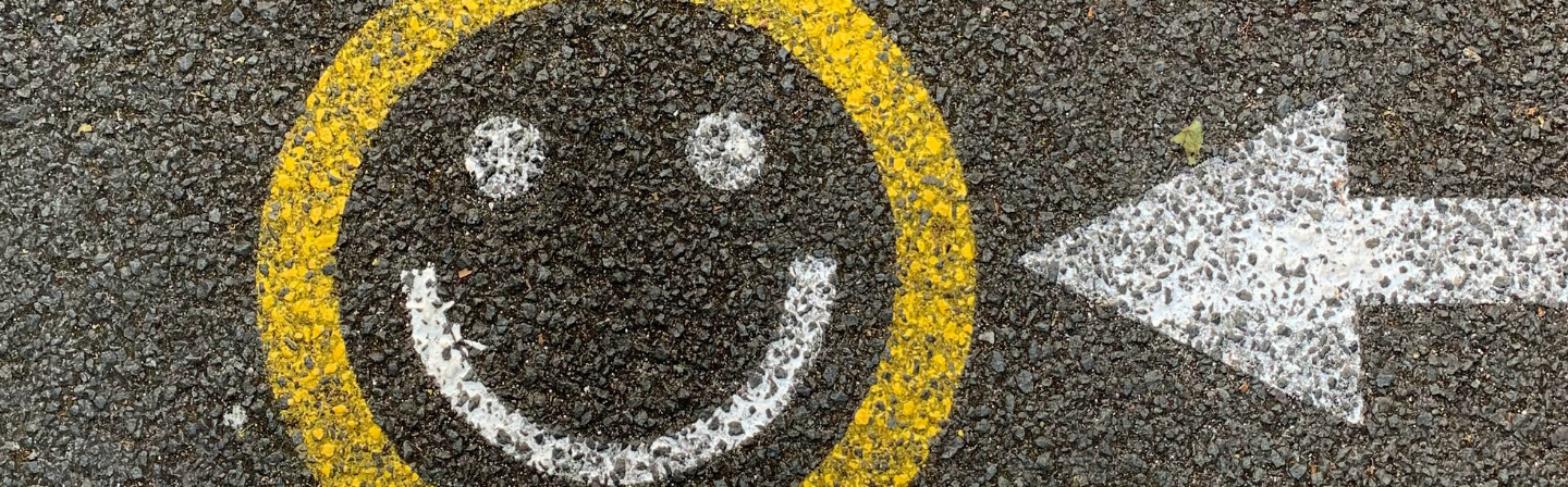 Flecha apuntando carita feliz en el asfalto.